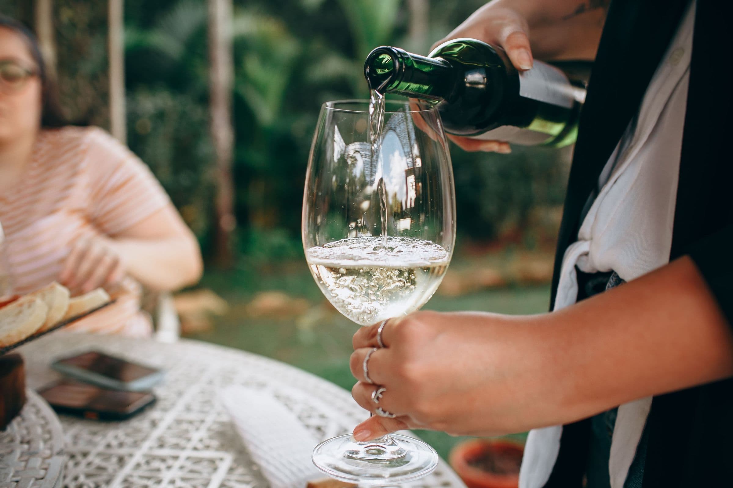 Weißwein wird bei einem Treffen im Garten ins Glas geschenkt